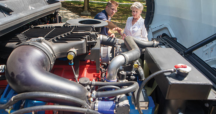 A man and woman looking down upon the engine of the H2-ICE demonstration vehicle.