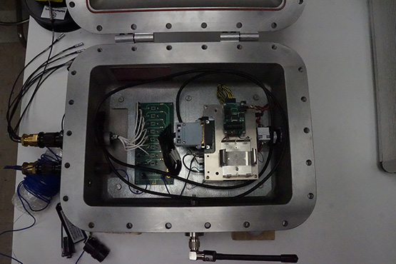 Completed instrument prototype with the lid open. The Wi-Fi antenna is attached to the front exterior of the enclosure; ultrasonic sensor cables and a thermocouple cable are attached to the left side of the enclosure.