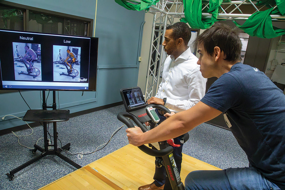 Man on stationery bike with a man next to him looking at ENABLE on the screen.