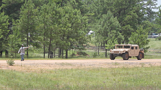 Photo of a military truck on dirt road with a man pointing at it.