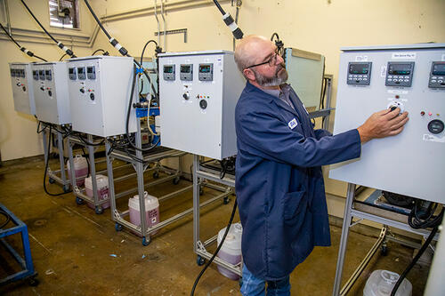 Man in blue lab coat adjusting dials on ASTM D2570 simulated service rig