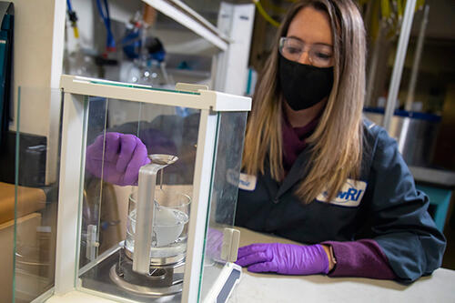 masked woman in blue lab coat performing volume swell and mass change testing