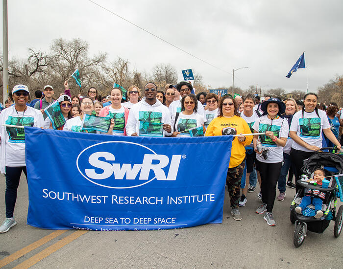 group of SwRI employees wearing matching MLK shirts standing behind a blue with white text Southwest Research Institute banner 