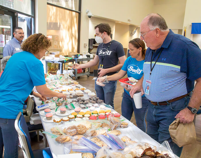 woman in blue shirt arranging baked goods as 2 men and a woman make purchases