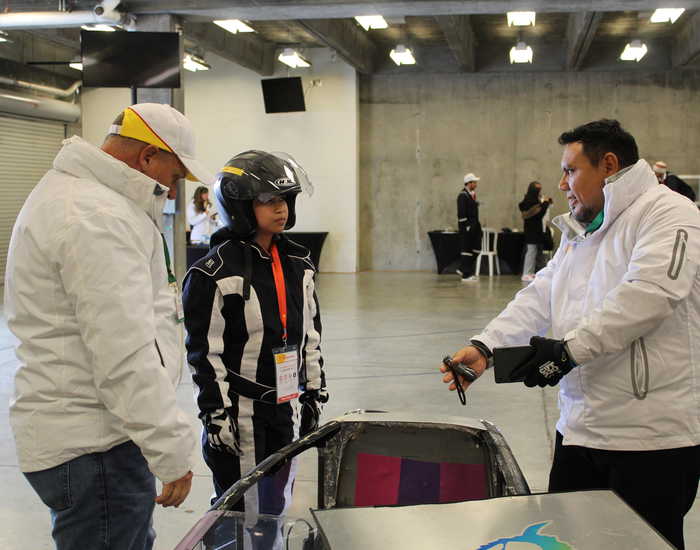 Two male SwRI staff providing technical and engineering support to student in driving gear for the Shell-Eco Marathon engineering competition
