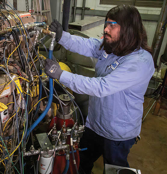 A worker with safety glasses stands next to a Low NOx Engine while working on it.