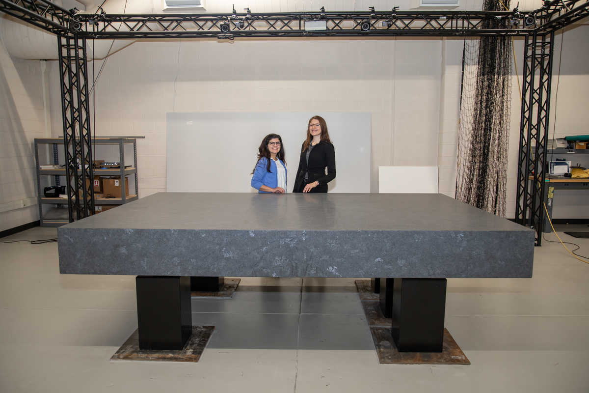 Towler and Wallace stand behind a fine-finish granite slab used to float robots and other samples using air bearings to simulate motion in a low-friction environment