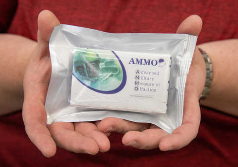 Two hands holding an Advanced Military Measure of Olfaction smell test kit