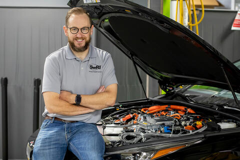 bearded man wearing glasses sitting on edge of car with hood open