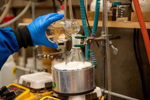 Blue gloved hand pouring liquid into test tube