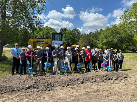 group of people wearing hard hats holding shovels with blue ribbons standing in front of construction equipment